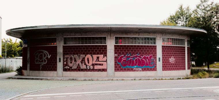 Ein rundes, flaches Gebäude weitwinklig fotografiert. Es wirkt wie ein umgedrehter Hut, da es oben eine Art Krempe 
besitzt. Es sind einige grossflächig getaggte Graffiti aufgebracht