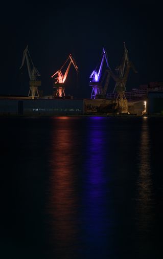 2 Kräne in der Nacht fotografiert, einer davon leuchtet orange, der andere violett