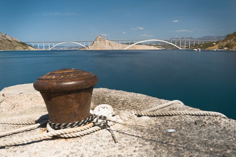 In der Ferne ist die Brücke zu sehen, während im Vordergrund prominent ein Poller ist, der zum Vertäuen von Booten 
genutzt wird