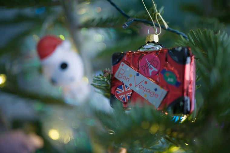 Ein Christbaum in Nahaufnahme, der Fokus ist auf eine "Christbaumkugel" in Form eines Reisekoffers. Auf ihm sind
mehrere Sticker angebracht: ein runder Sticker mit Union Jack, einer mit Paris und der Silhouette des Eiffelturms, 
ein rechteckiger auf dem "Bon Vojage" steht. Ausserhalb des Fokus, etwas hinterhalb des Koffers, sieht man eine 
weitere Christbaumkugel in Form von Kodama-Geistern aus Prinzessin Mononoke (dem Studio Ghibli 
Film)